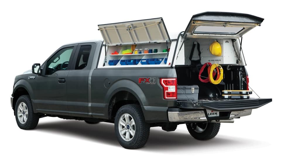 A gray pickup truck with its tailgate down, featuring customized storage in the bed. It includes shelves with colorful bins and various equipment, like hoses, neatly organized. 